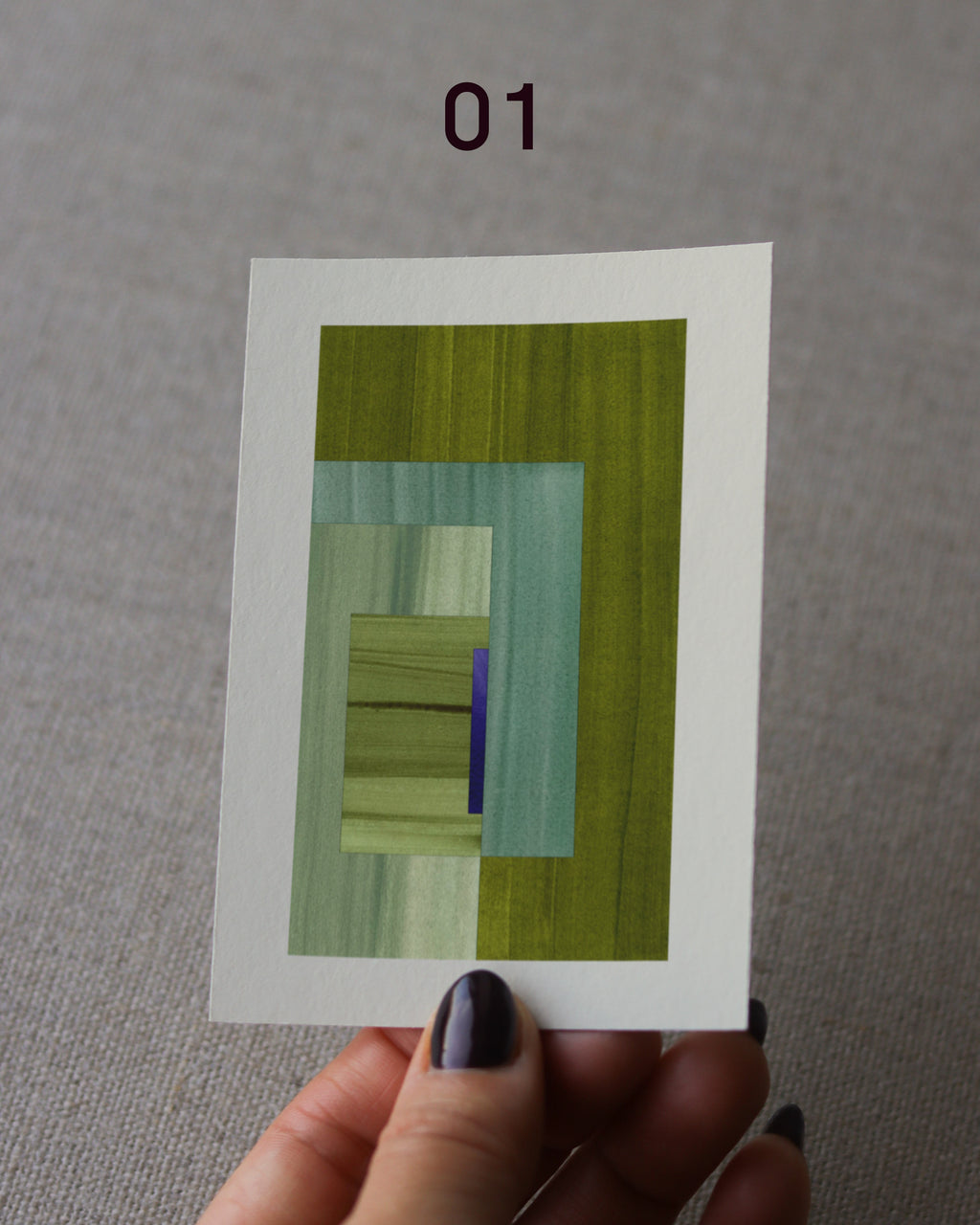 Hand holding an abstract art print sample, with a geometric style in moss green and turquoise.
