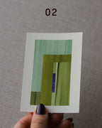 Hand holding an abstract art print sample, with a geometric style in moss green, turquoise and royal blue.