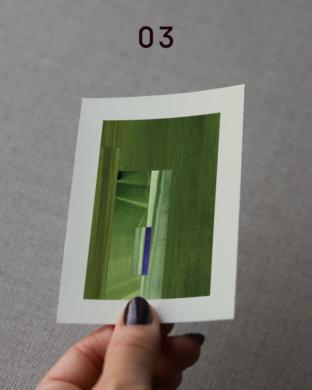 Hand holding an abstract art print sample, with a geometric style in olive green, moss green and blue.