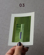 Hand holding an abstract art print sample, with a geometric style in olive green, moss green and blue.