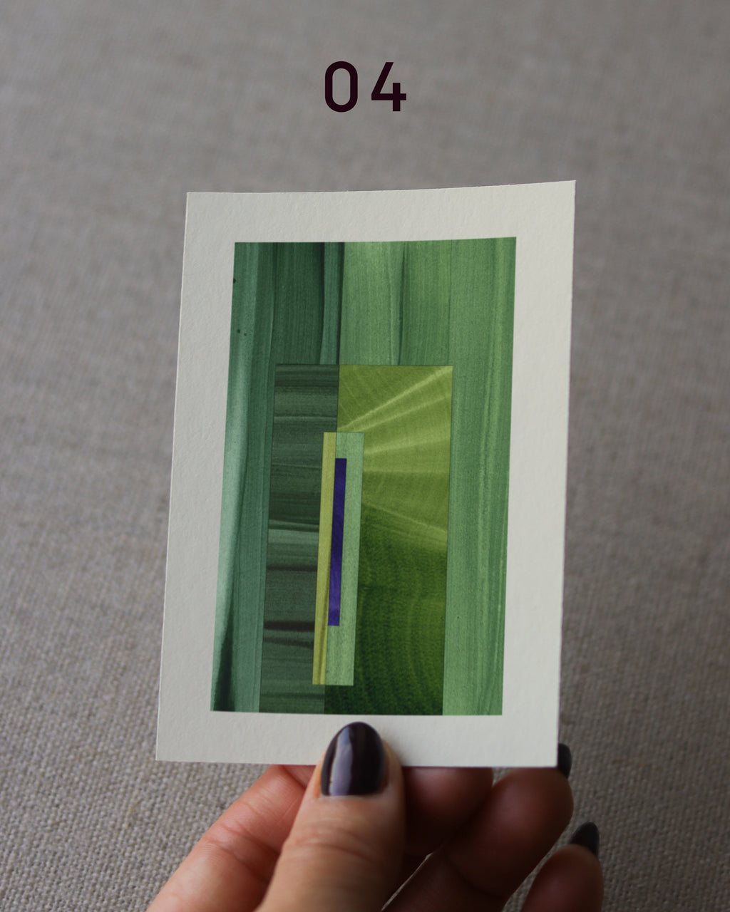 Hand holding an abstract art print sample, with a geometric style in grass green and royal blue.