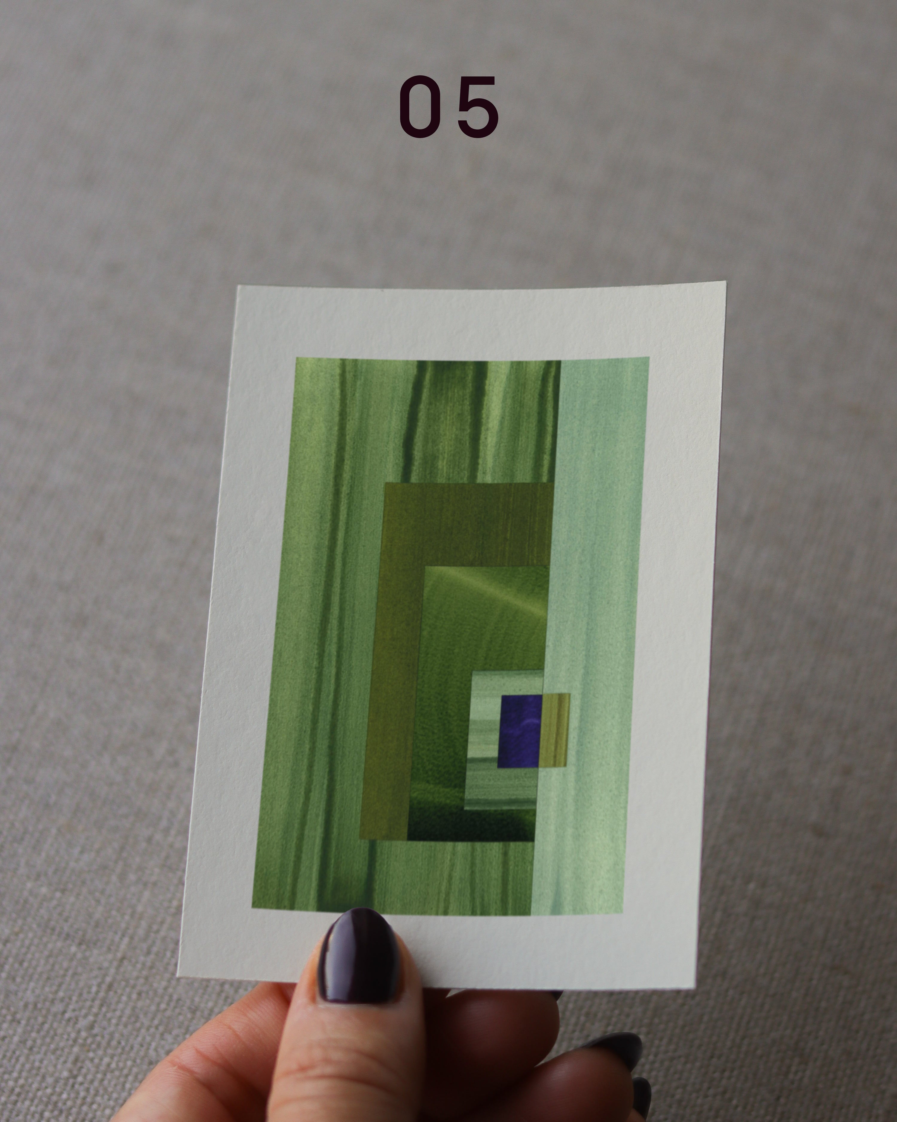 Hand holding an abstract art print sample, with a geometric style in moss green, mint green and royal blue.