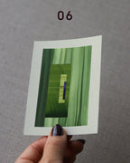 Hand holding an abstract art print sample, with a geometric style in moss and grass green and royal blue.