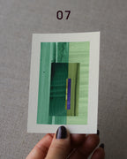 Hand holding an abstract art print sample, with a geometric style in mint and sage green, turquoise and forest green.