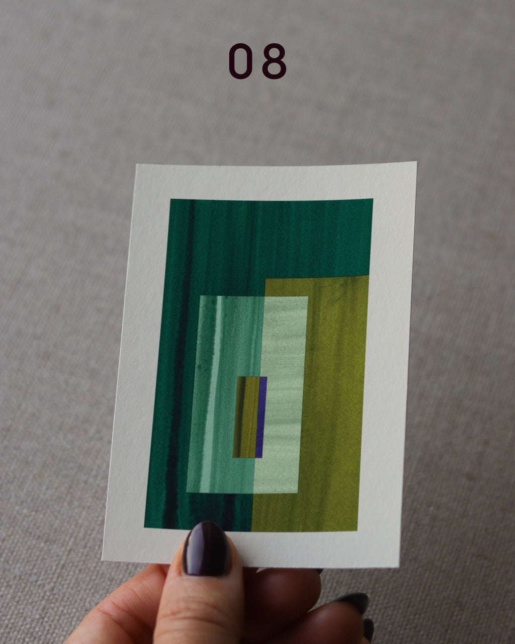 Hand holding an abstract art print sample, with a geometric style in moss green, forest green and turquoise.
