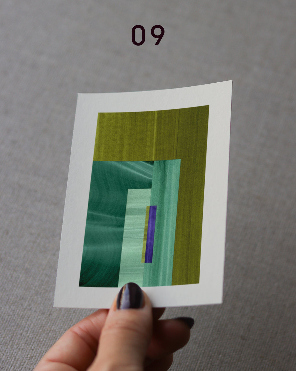 Hand holding an abstract art print sample, with a geometric style in moss green and turquoise.