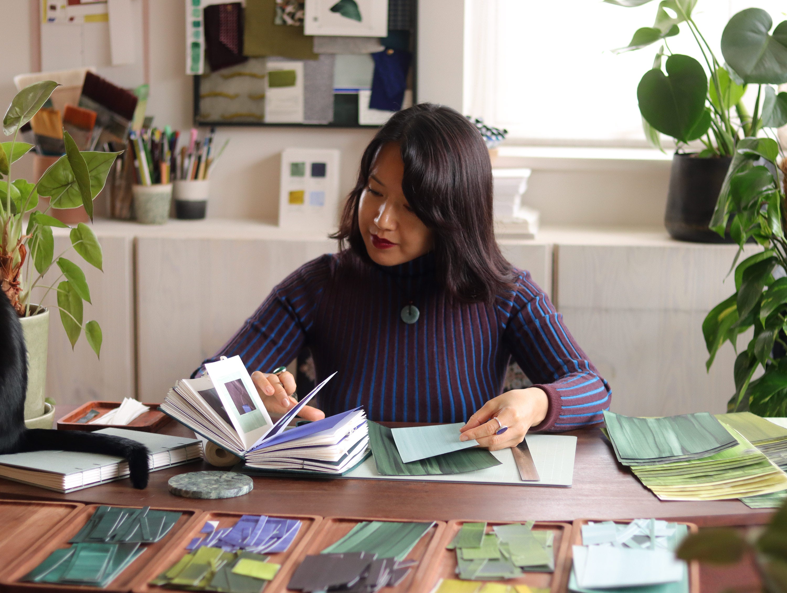 Abstract artist Aimee Johanan working on artwork at a desk, surround by art materials, painted papers and plants