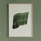 Leafy, deep green abstract artwork in a thin white oak wooden frame on a sage green wall