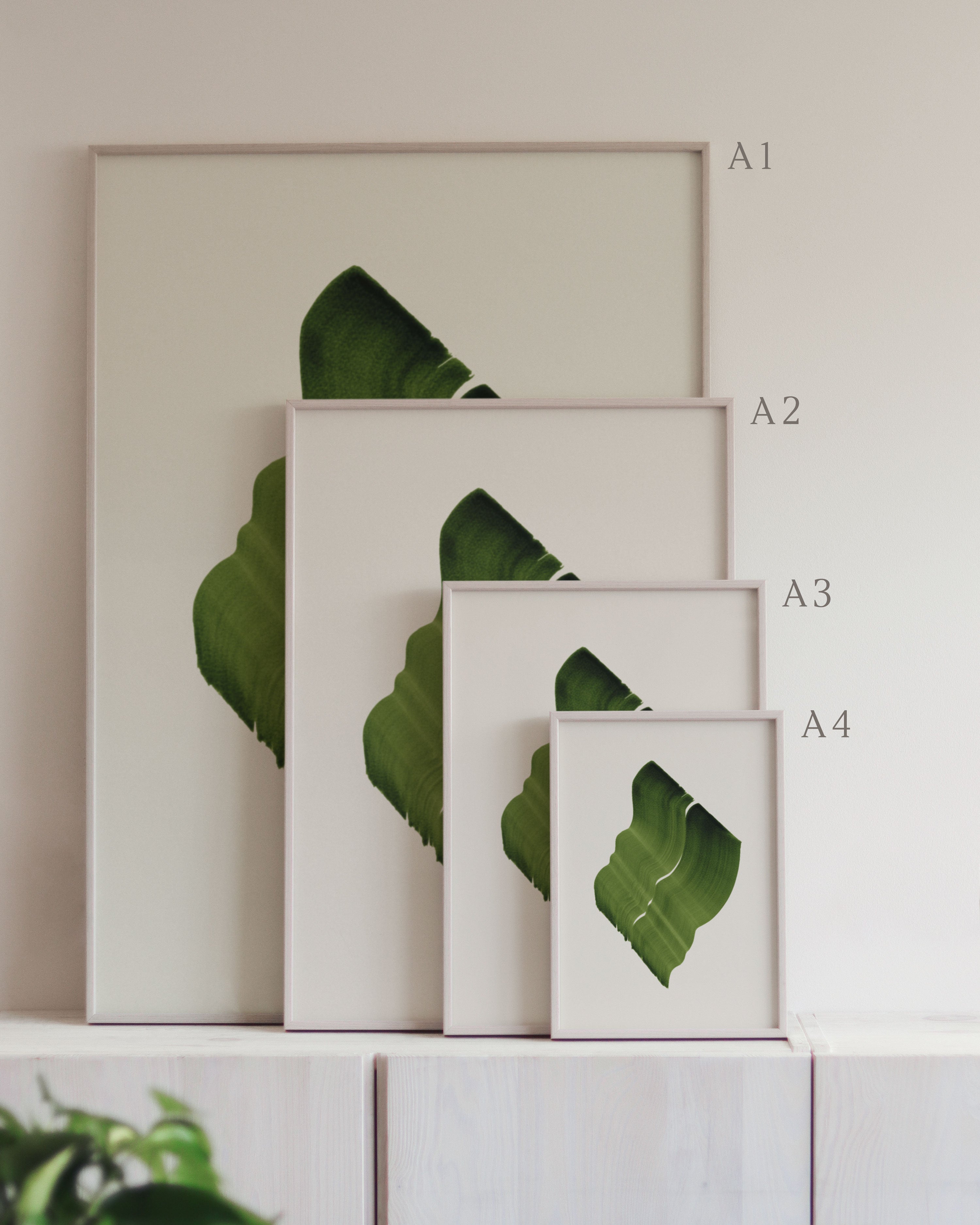 Set of framed green art prints with abstract leaf designs on a neutral background, showing in sizes A4, A3, A2 and A1