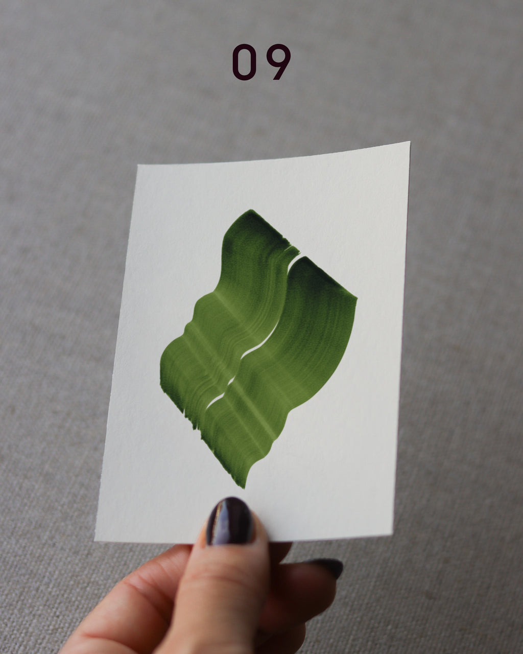 Hand holding sample of a green abstract art print with a green leaf-like design