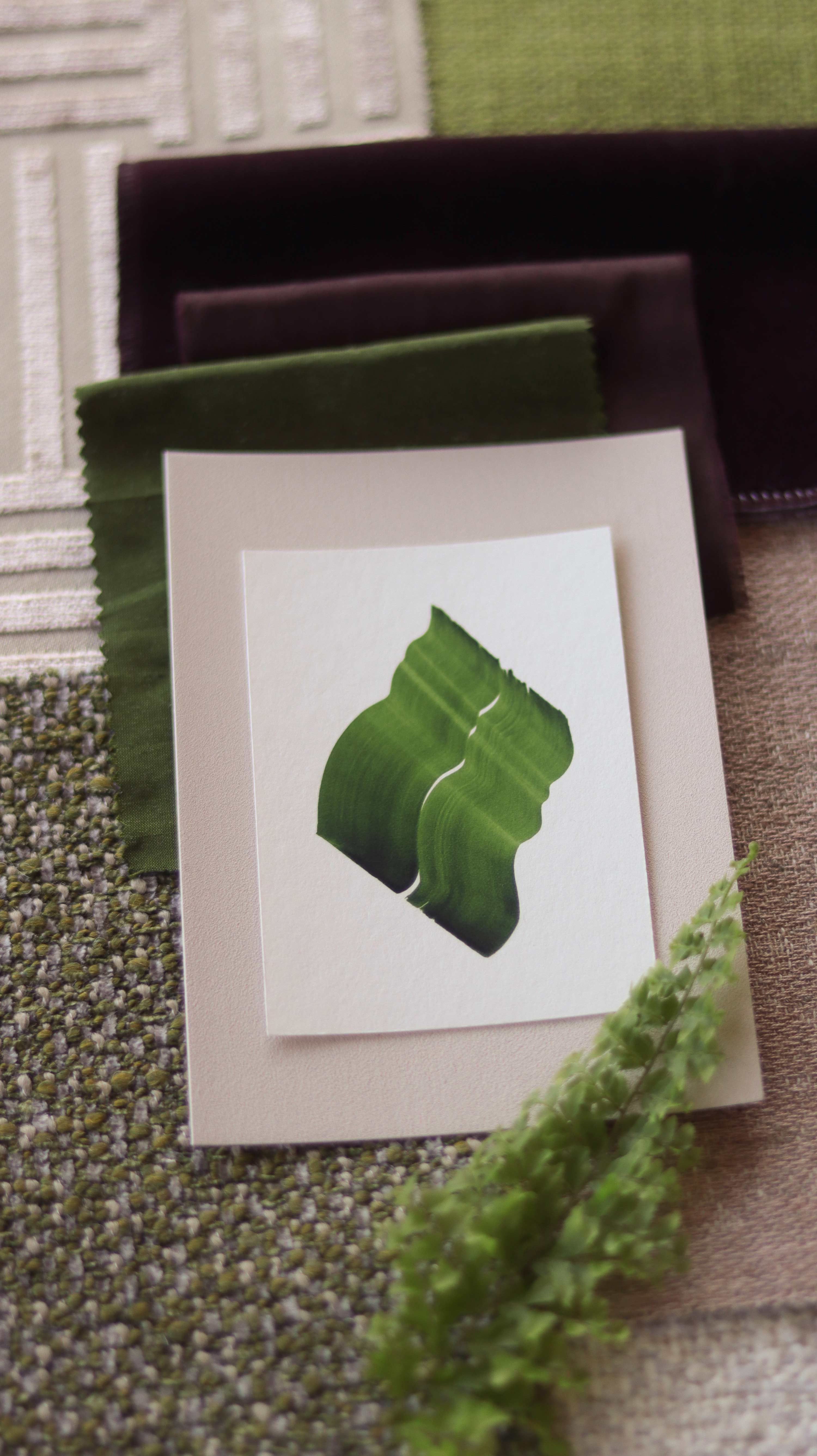 Green abstract art print sample with a green leaf-like design on a textured paint swatch with fabric swatches. Inspiration for spring green and blush pink themed interior design.