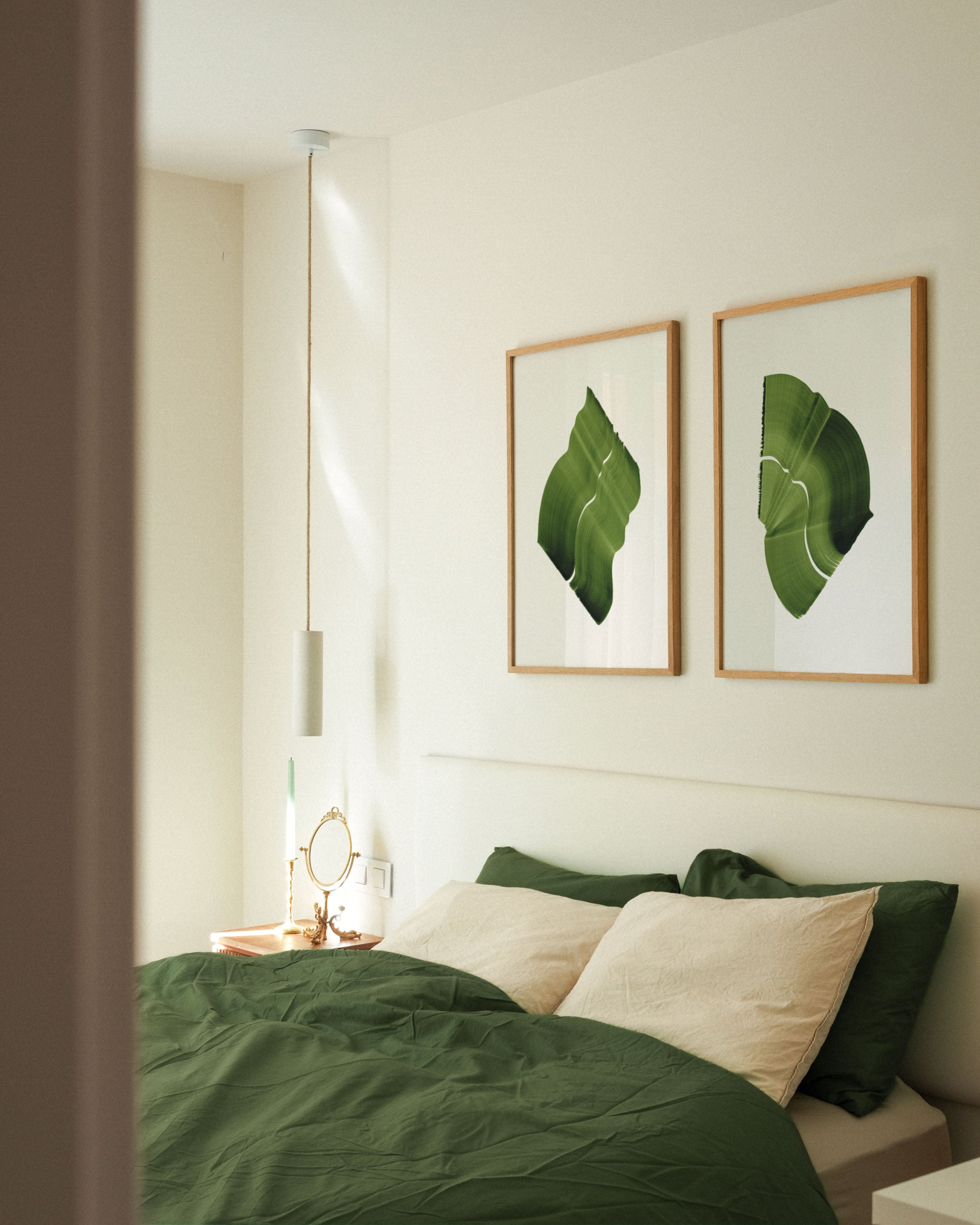 Pair of green abstract paintings with flowing botanical leaf-like shapes, hung in oak frames in a modern, minimal bedroom with green linen bedding