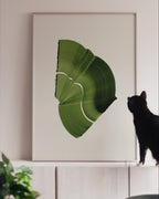 Large green art print in a white oak frame, on white cabinets with a black cat looking at it