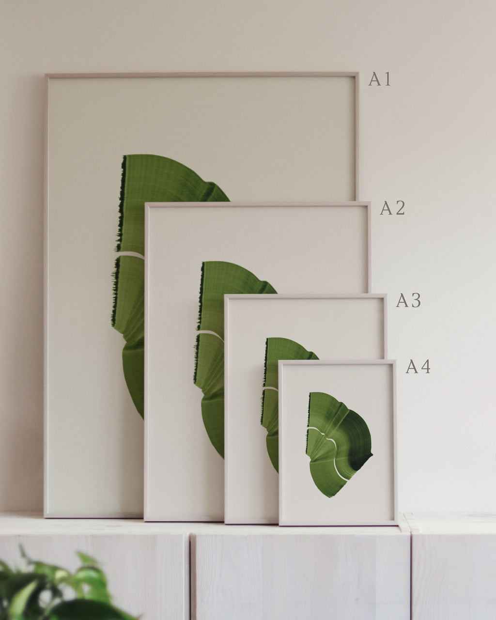 Set of framed green art prints with abstract leaf designs on a neutral background, showing in sizes A4, A3, A2 and A1