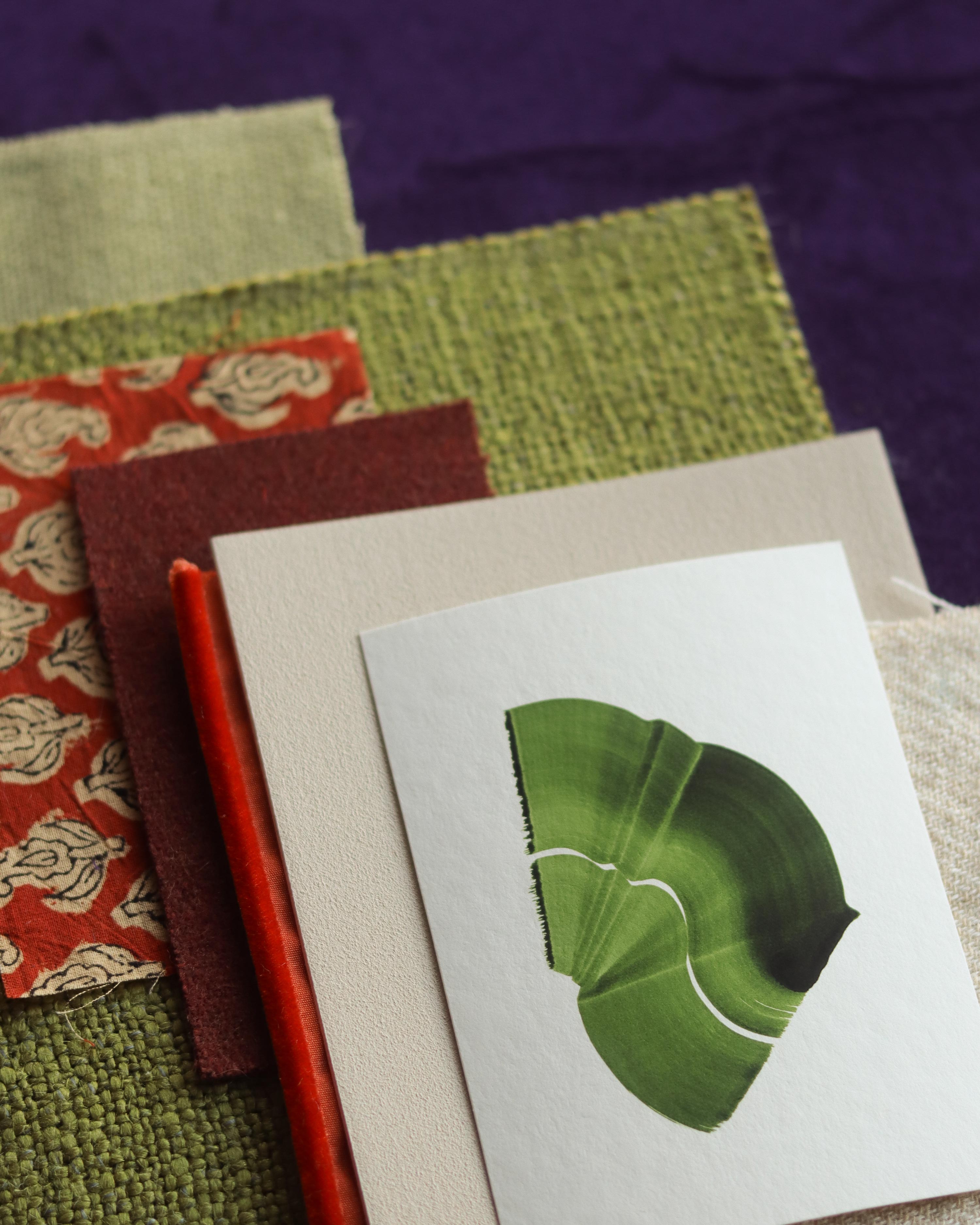 Green abstract art print sample with a green leaf-like design on a textured paint swatch with fabric swatches. Inspiration for green and burnt orange themed interior decor.