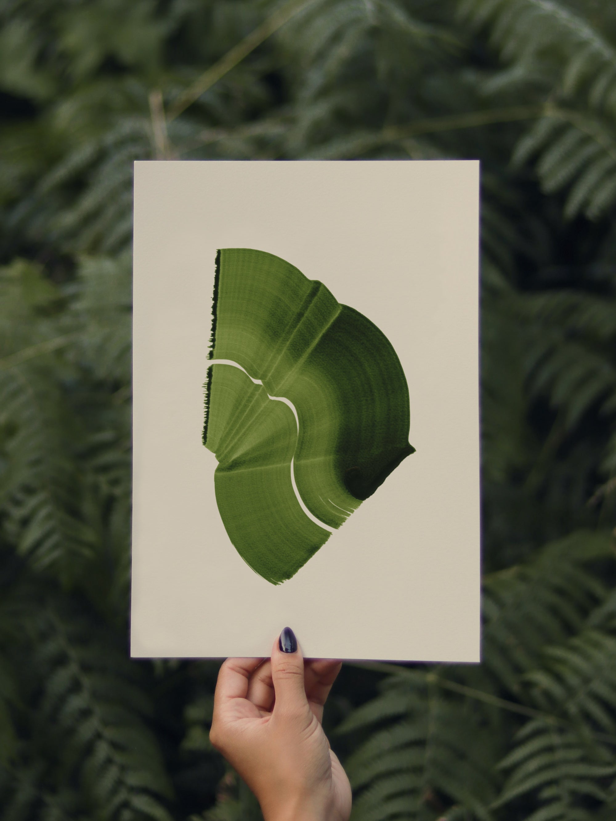 Hand holding a green abstract leaf-shaped print, against a green leafy background in the forest