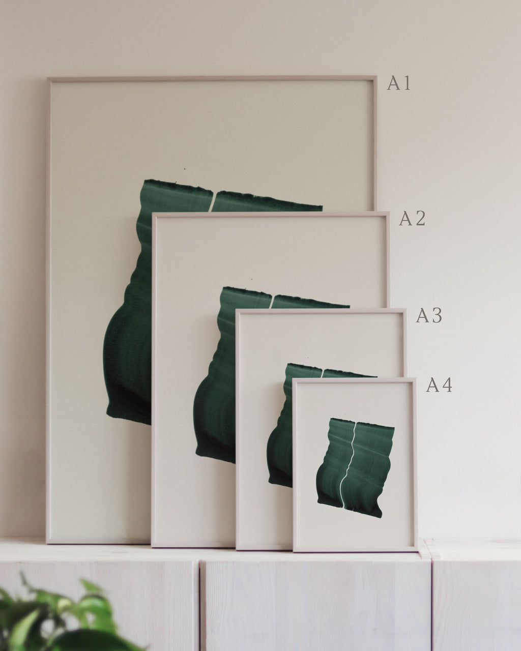 Set of framed green art prints with abstract leaf designs on a neutral background, showing in sizes A4, A3, A2 and A1