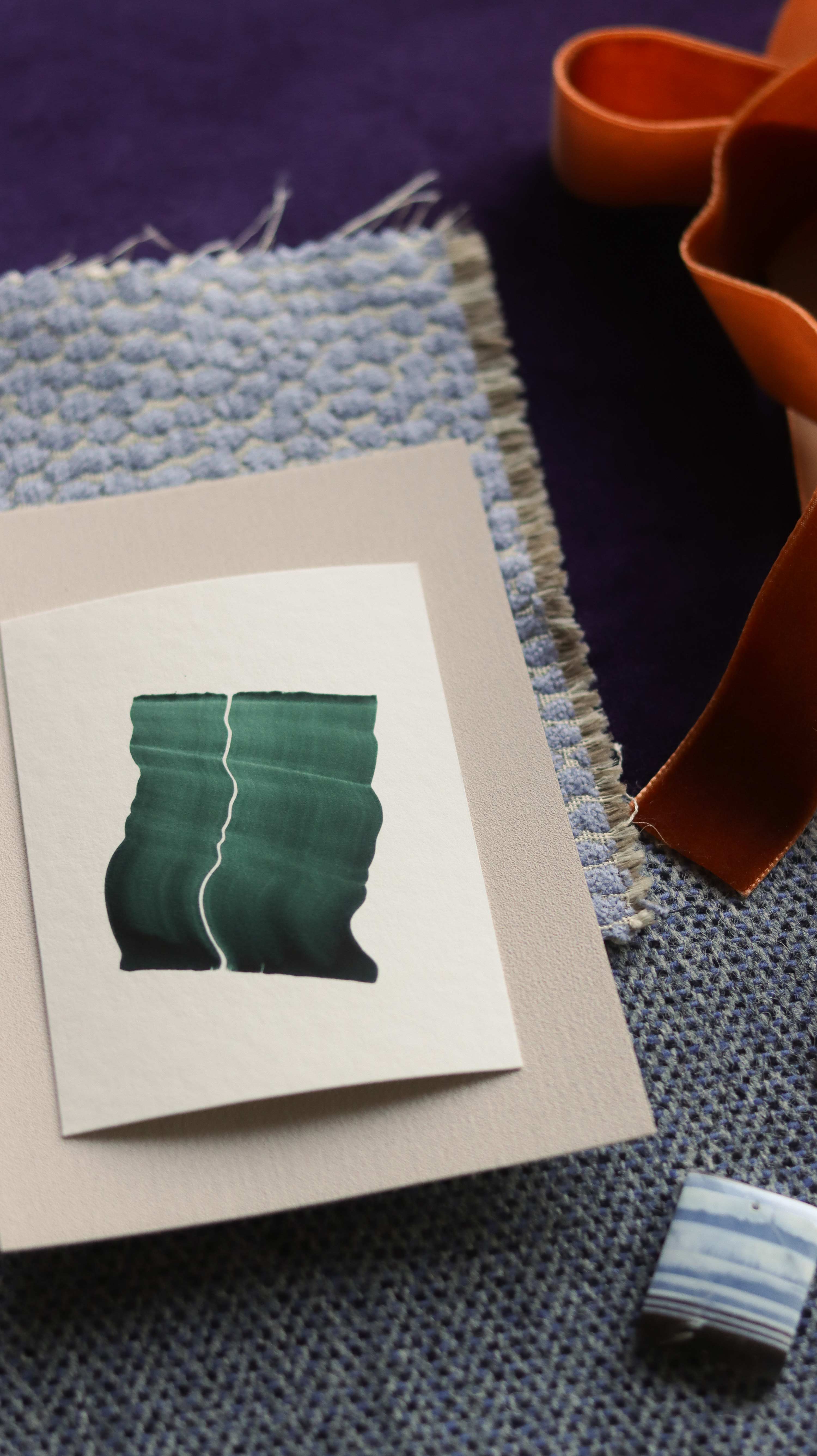 Green abstract art print sample with a green leaf-like design on a textured paint swatch with fabric swatches. Inspiration for blush pink, dusty blue and ink purple themed interior decor.