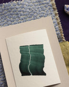 Dark green abstract art print sample with a green leaf-like design on a textured paint swatch with fabric swatches. Inspiration for green and blue themed interior decor.