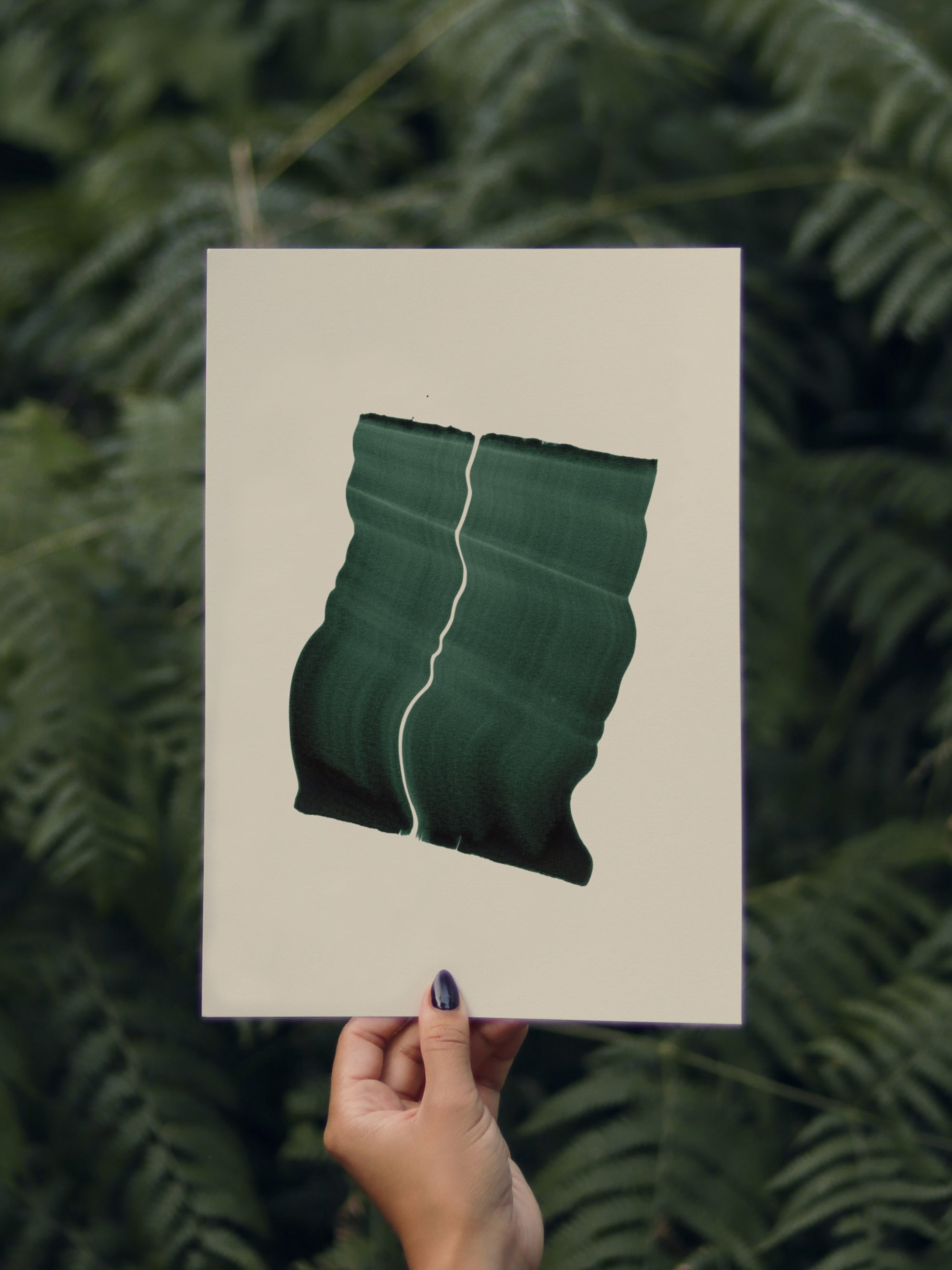 Hand holding a green abstract leaf-shaped print, against a green leafy background in the forest