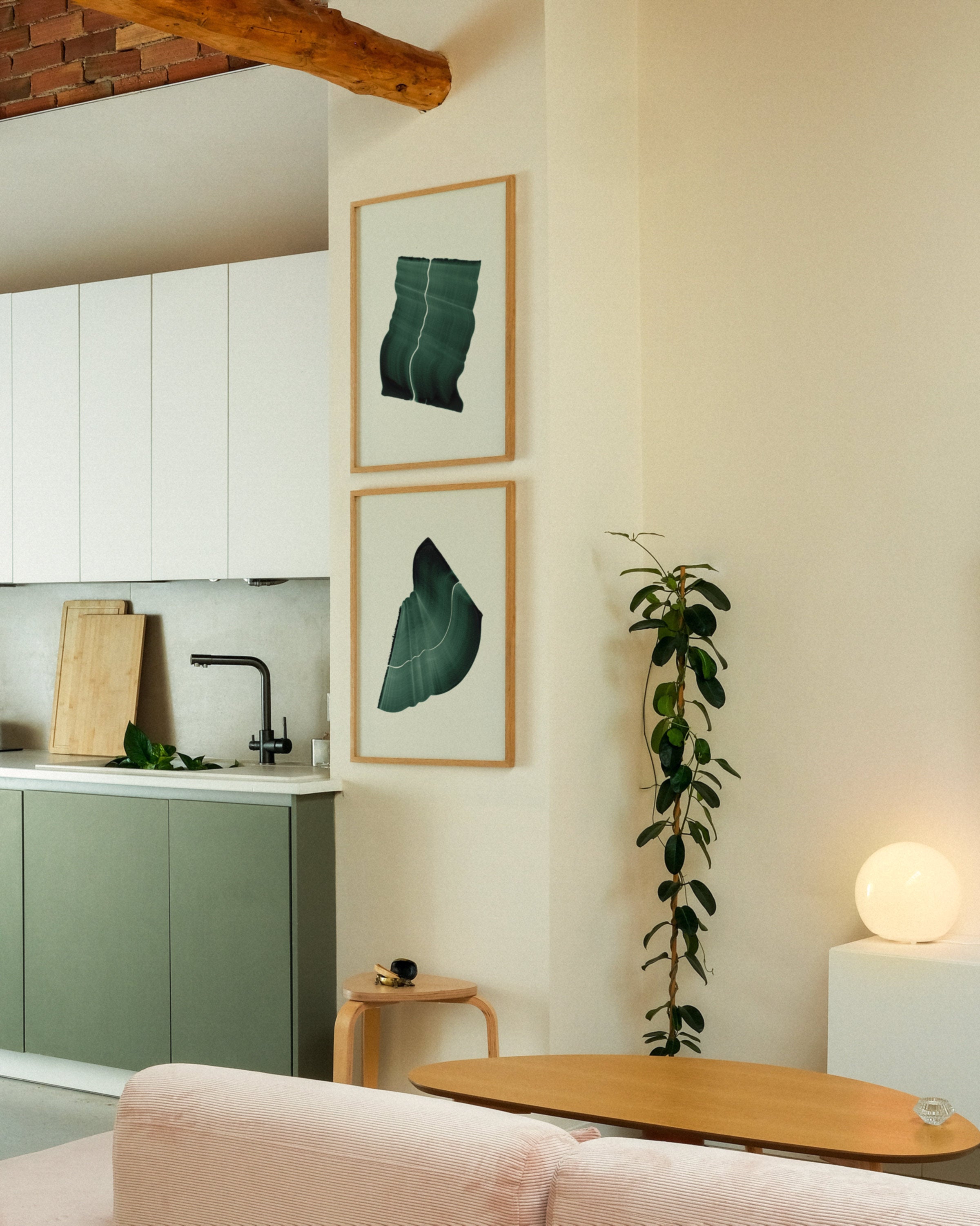 Modern kitchen with green cabinets, framed green abstract leaf-like art, and a plant.
