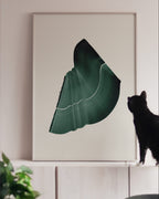 Large green art print in a white oak frame, on white cabinets with a black cat looking at it
