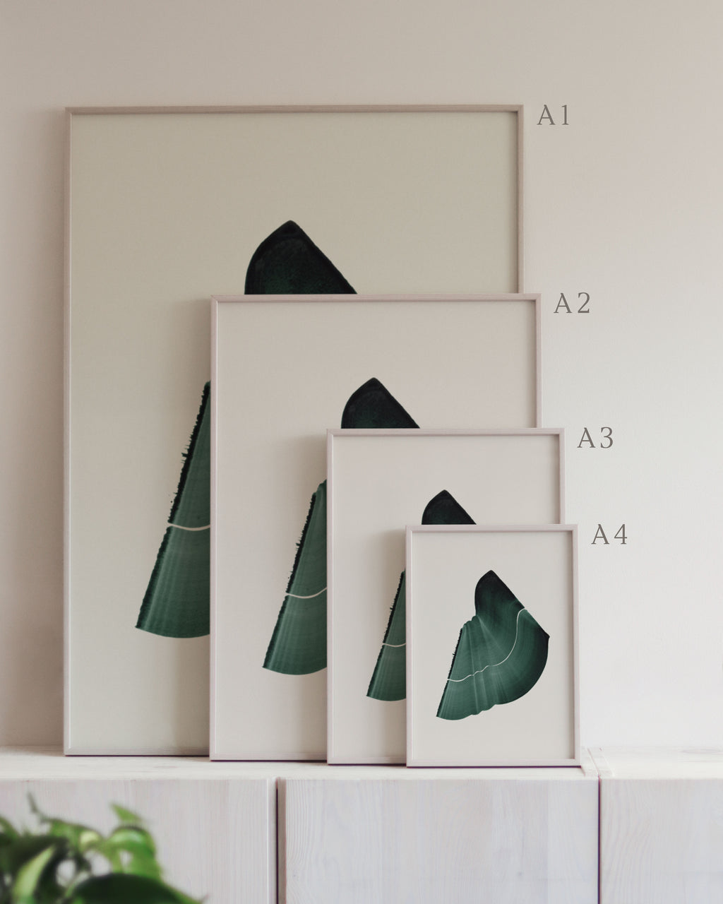 Set of framed green art prints with abstract leaf designs on a neutral background, showing in sizes A4, A3, A2 and A1