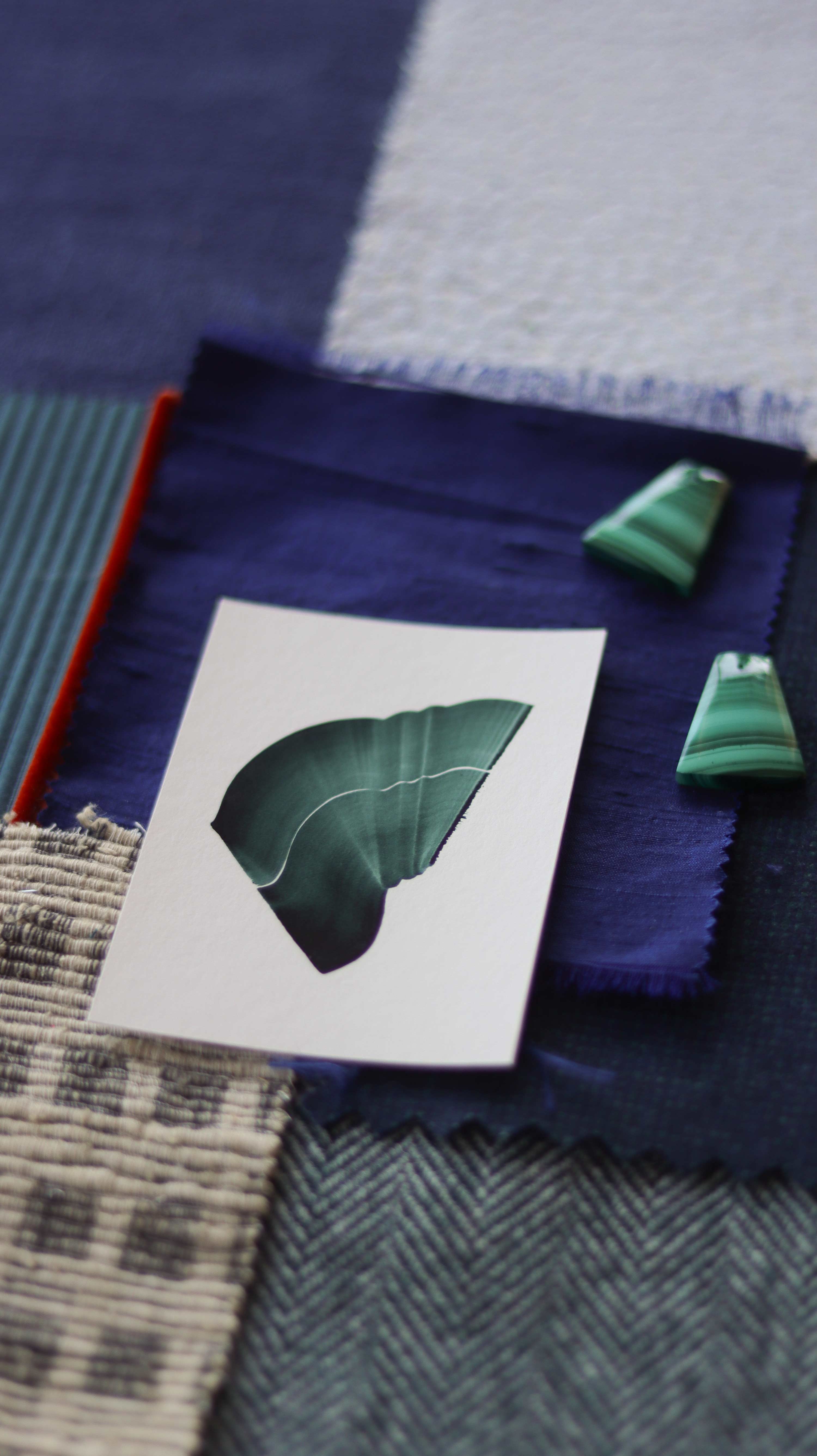 Green abstract art print sample with a green leaf-like design on a textured paint swatch with fabric swatches. Inspiration for cobalt Klein blue and teal themed interior decor.