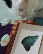 Green abstract art print sample with a green leaf-like design on a textured paint swatch with fabric swatches. Inspiration for teal, blue and orange themed interior decor.