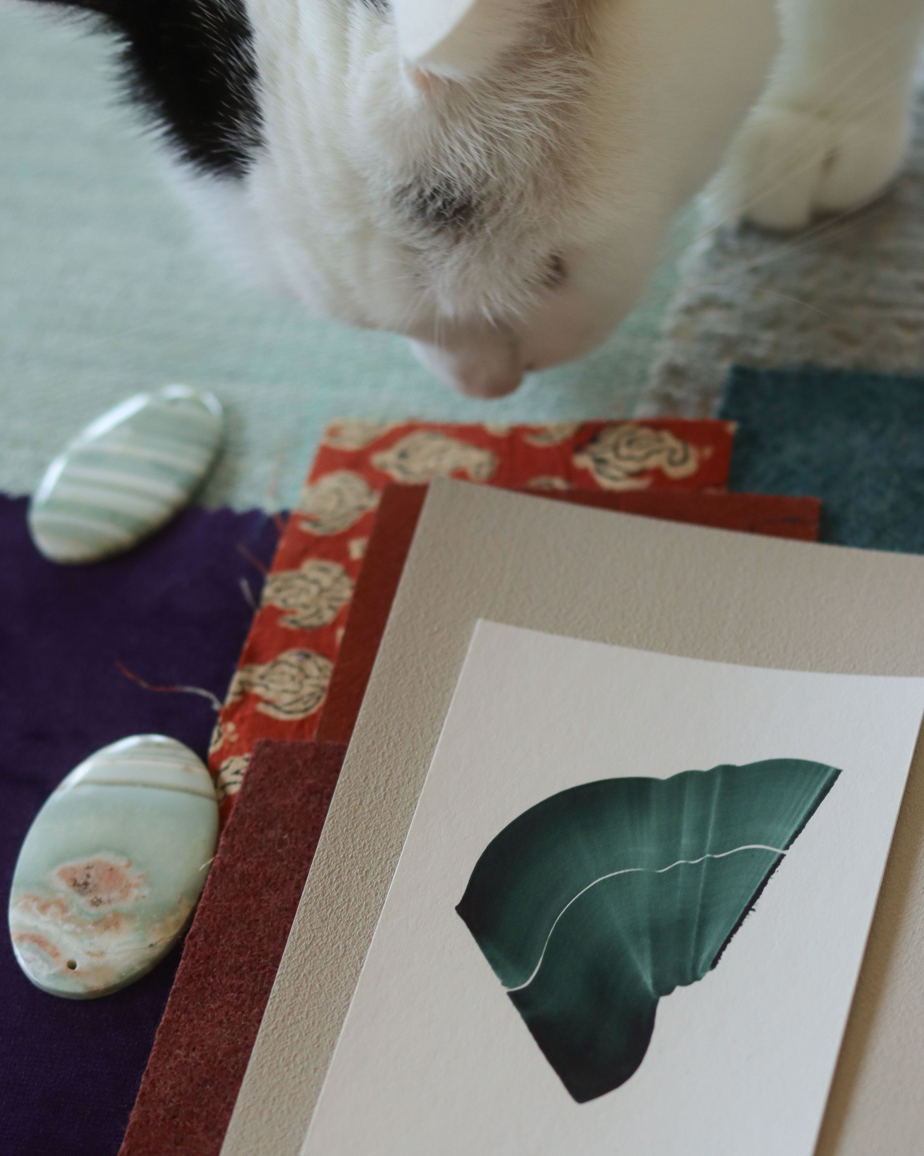Green abstract art print sample with a green leaf-like design on a textured paint swatch with fabric swatches. Inspiration for teal, blue and orange themed interior decor.
