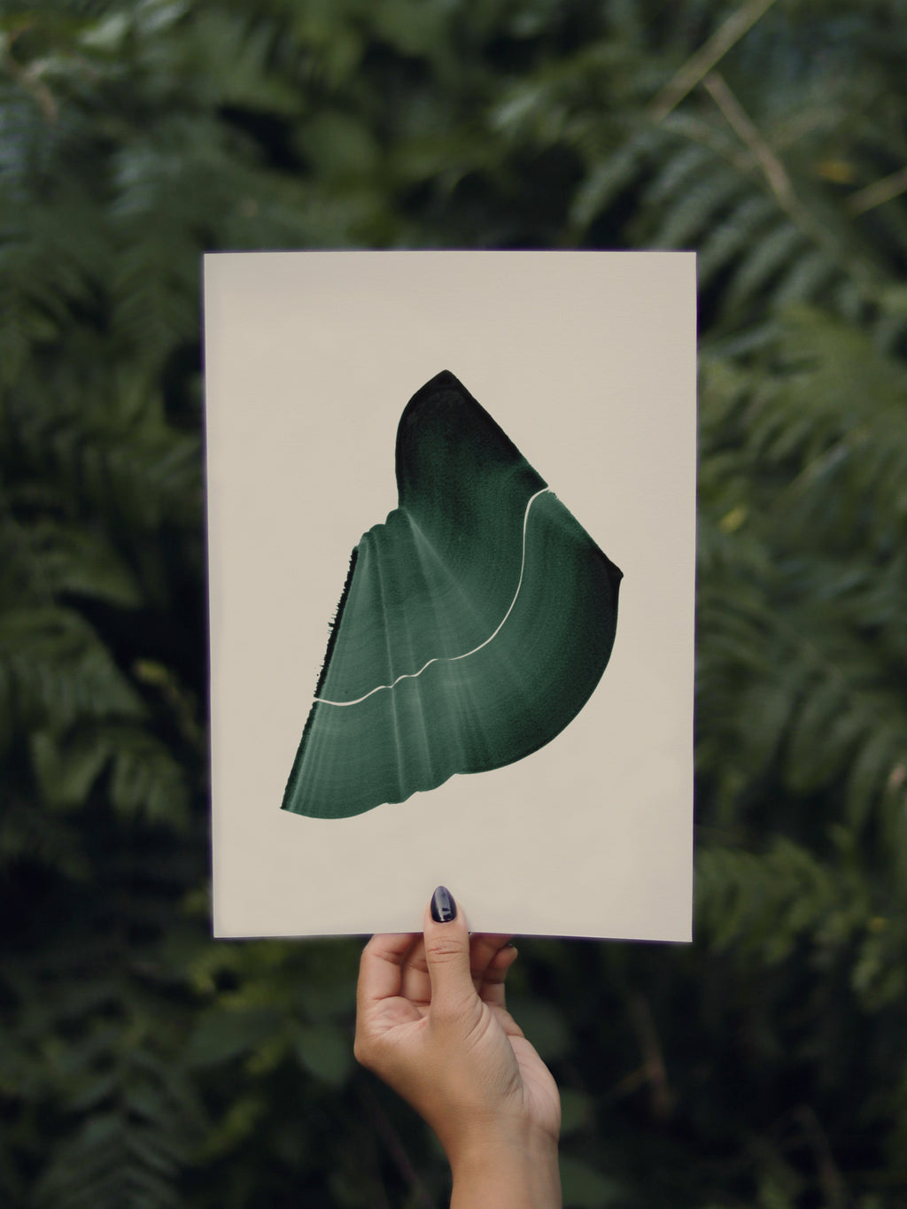 Hand holding a green abstract leaf-shaped print, against a green leafy background in the forest