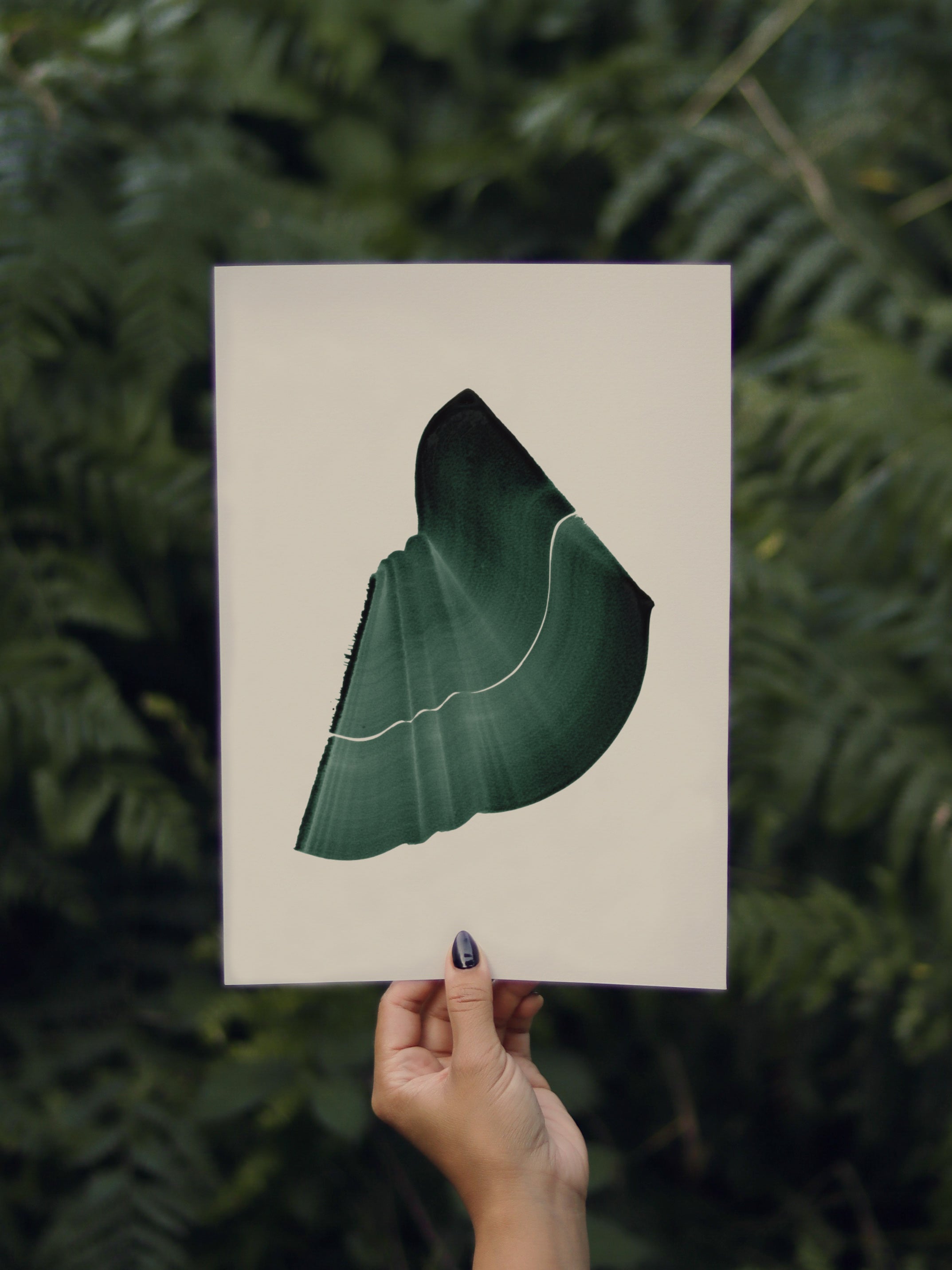 Hand holding a green abstract leaf-shaped print, against a green leafy background in the forest