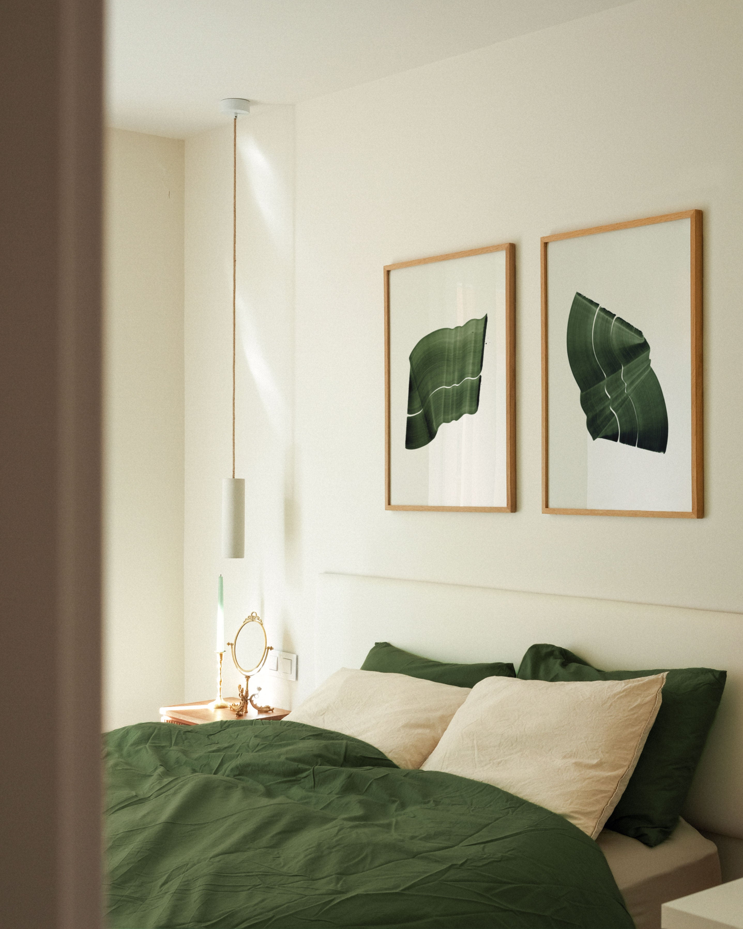 Pair of green abstract paintings with flowing botanical leaf-like shapes, hung in oak frames in a modern, minimal bedroom with green linen bedding