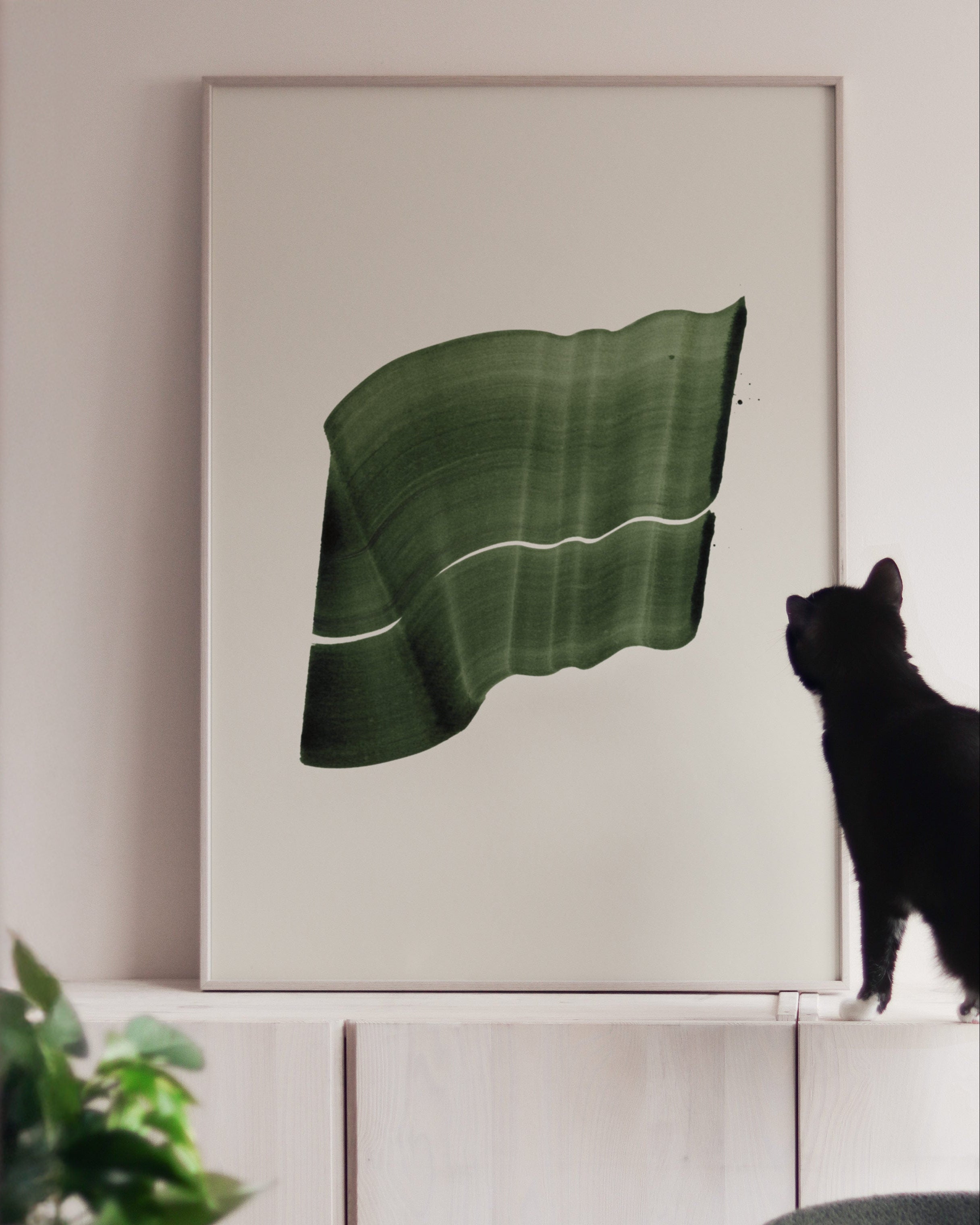 Large green art print in a white oak frame, on white cabinets with a black cat looking at it