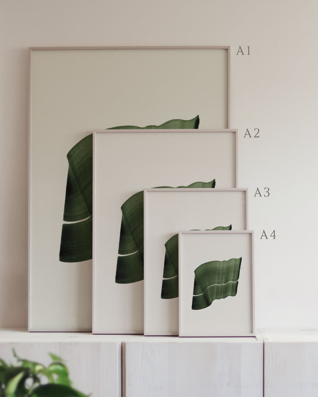 Set of framed green art prints with abstract leaf designs on a neutral background, showing in sizes A4, A3, A2 and A1