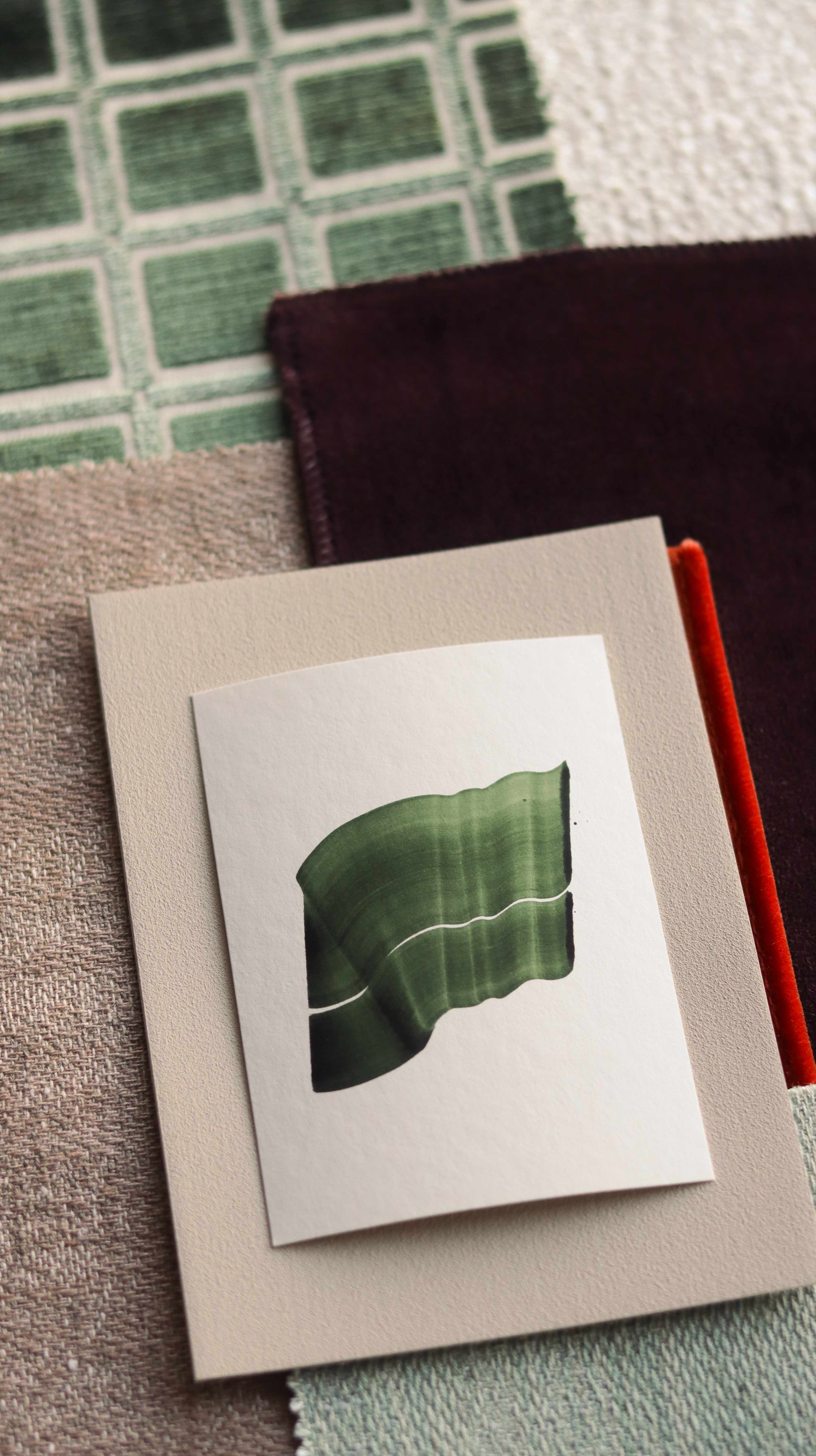 Green abstract art print sample with a green leaf-like design on a textured paint swatch with fabric swatches. Inspiration for blush pink, sage green and burgundy themed interior decor.