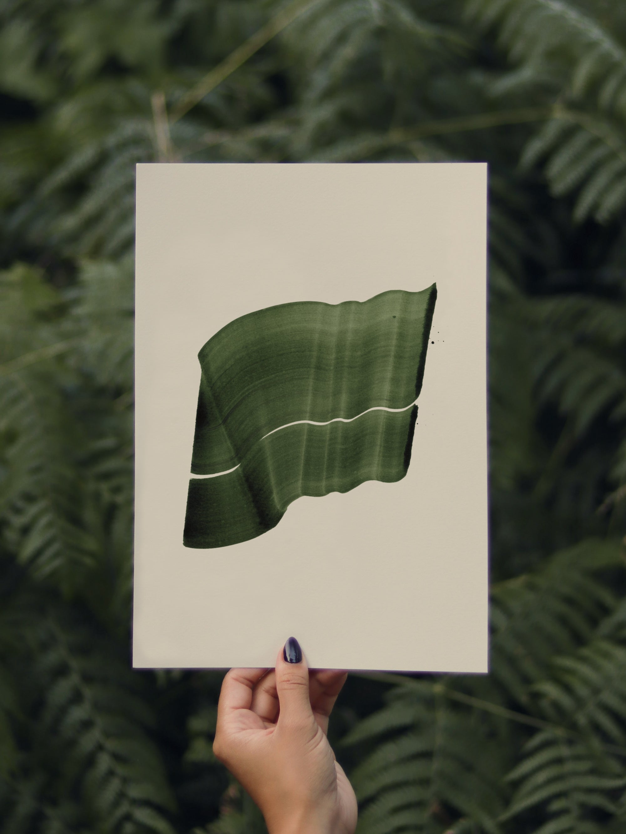 Hand holding a green abstract leaf-shaped print, against a green leafy background in the forest
