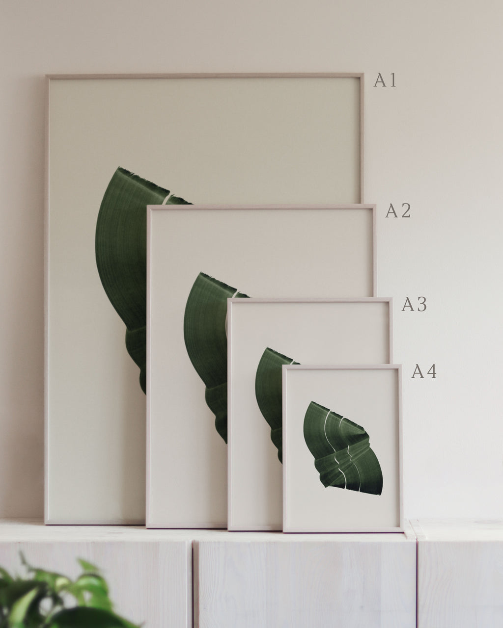 Set of framed green art prints with abstract leaf designs on a neutral background, showing in sizes A4, A3, A2 and A1