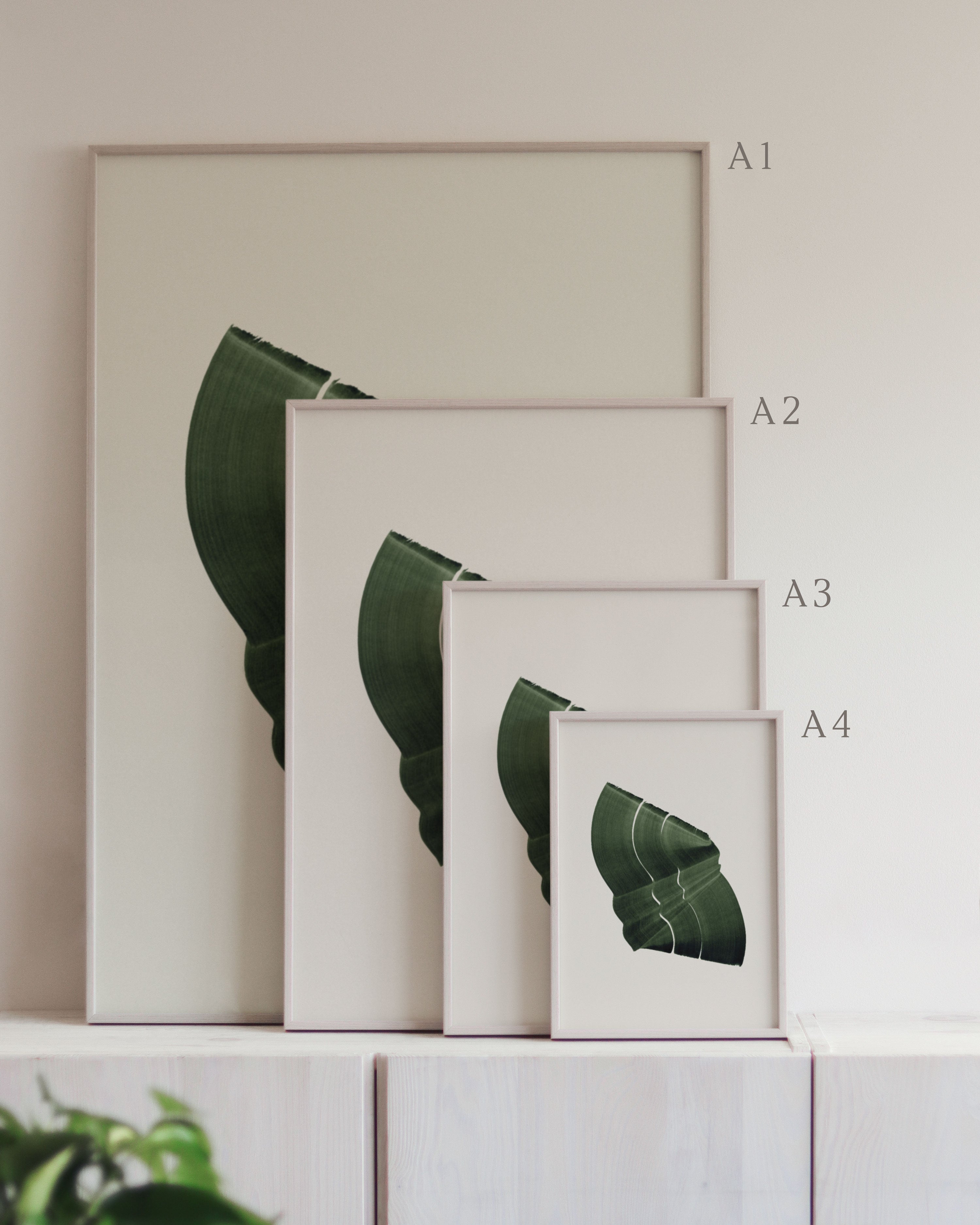 Set of framed green art prints with abstract leaf designs on a neutral background, showing in sizes A4, A3, A2 and A1