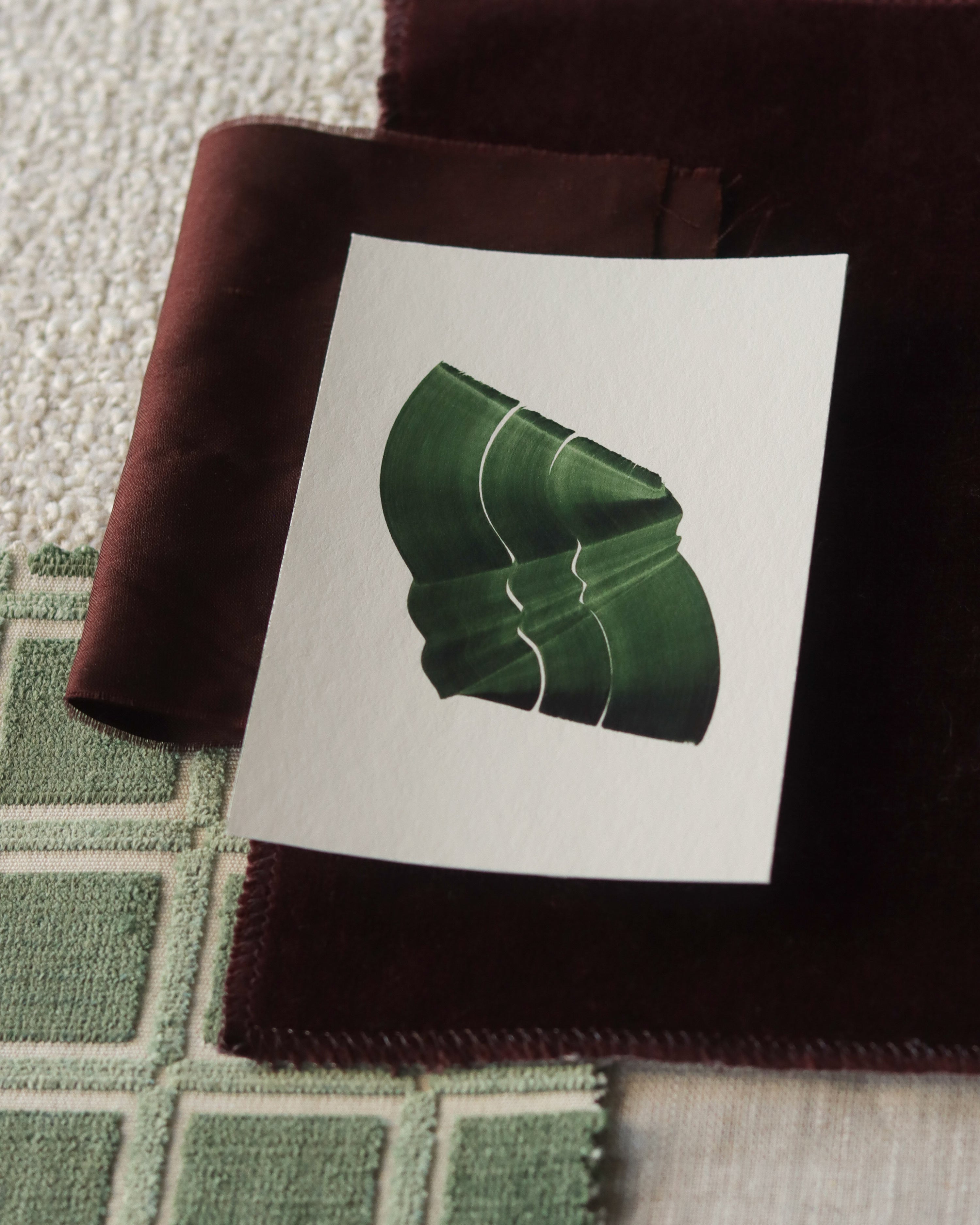Green abstract art print sample with a green leaf-like design on a textured paint swatch with fabric swatches. Inspiration for green and brown themed interior decor.
