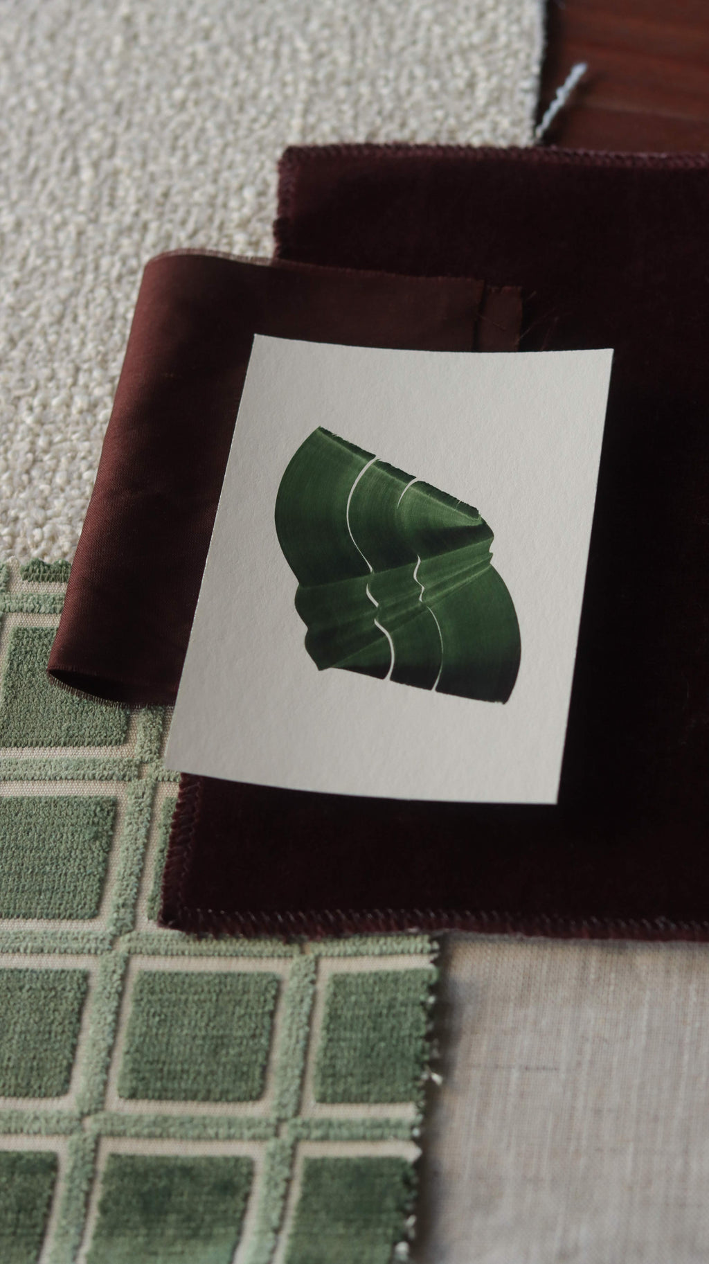 Green abstract art print sample with a green leaf-like design on a textured paint swatch with fabric swatches. Inspiration for sage green and burgundy themed interior decor.