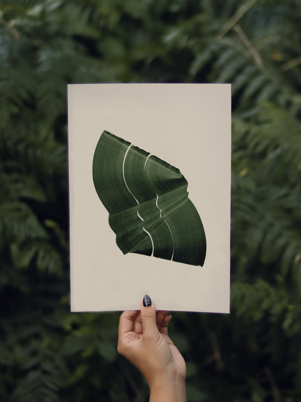 Hand holding a green abstract leaf-shaped print, against a green leafy background in the forest