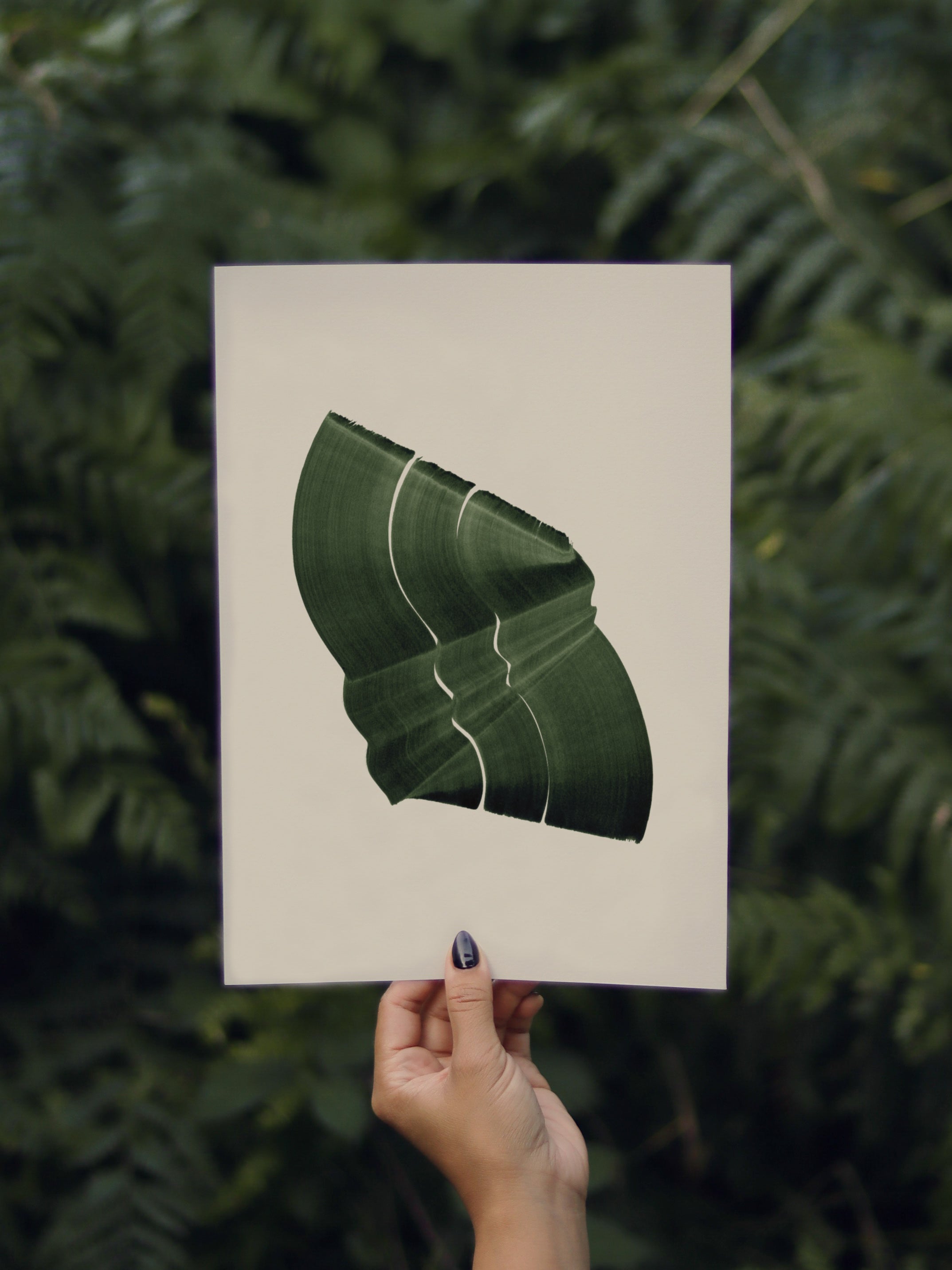 Hand holding a green abstract leaf-shaped print, against a green leafy background in the forest