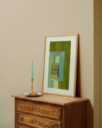 Framed moss green and turquoise abstract artwork on a wooden dresser against a beige wall