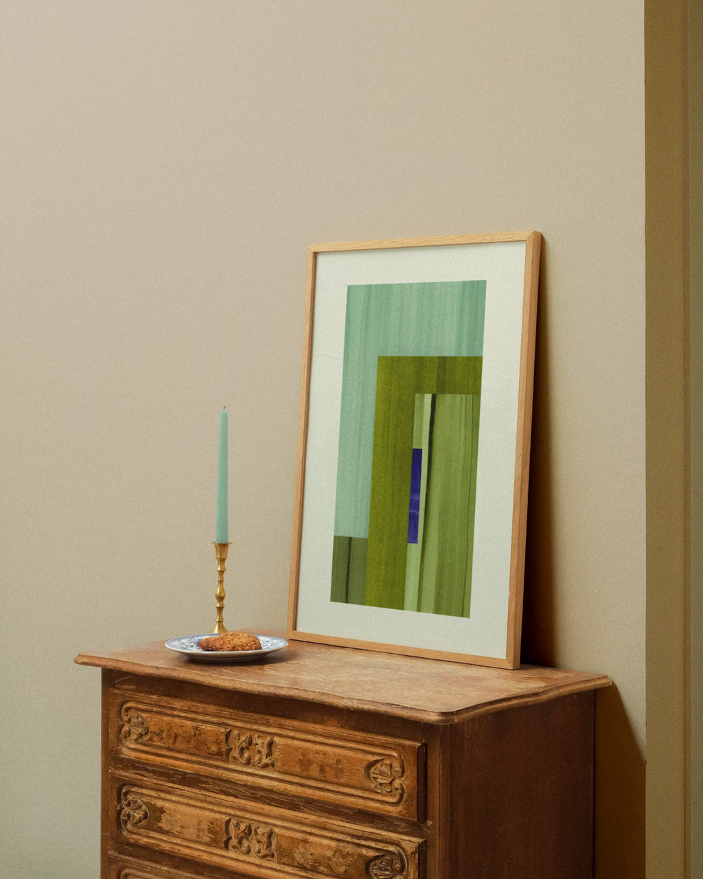 Framed moss green and turquoise abstract artwork on a wooden dresser against a beige wall