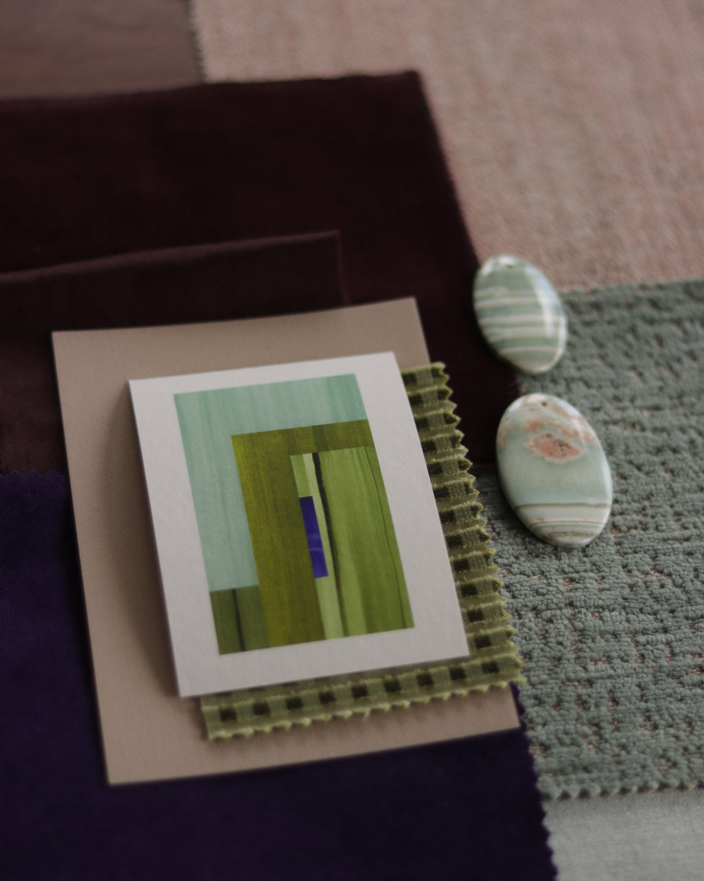 Colourful green interiors inspiration: Small geometric abstract art print sample with moss green, turquoise and blue colours, laying on top of fabric swatches.