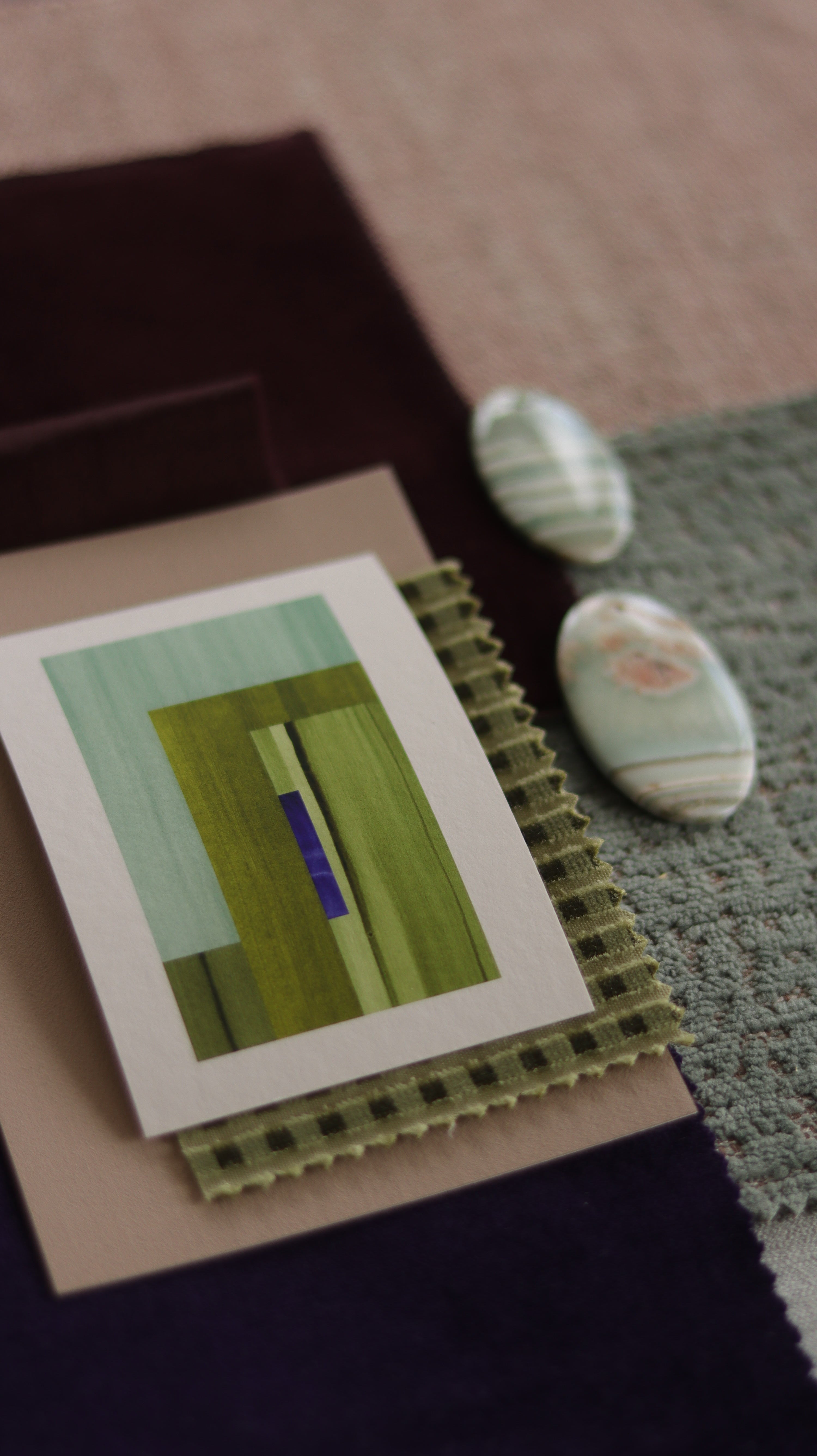 Small abstract art print sample with moss green, turquoise and blue colours, laying on top of fabric swatches for colourful  interiors inspiration.