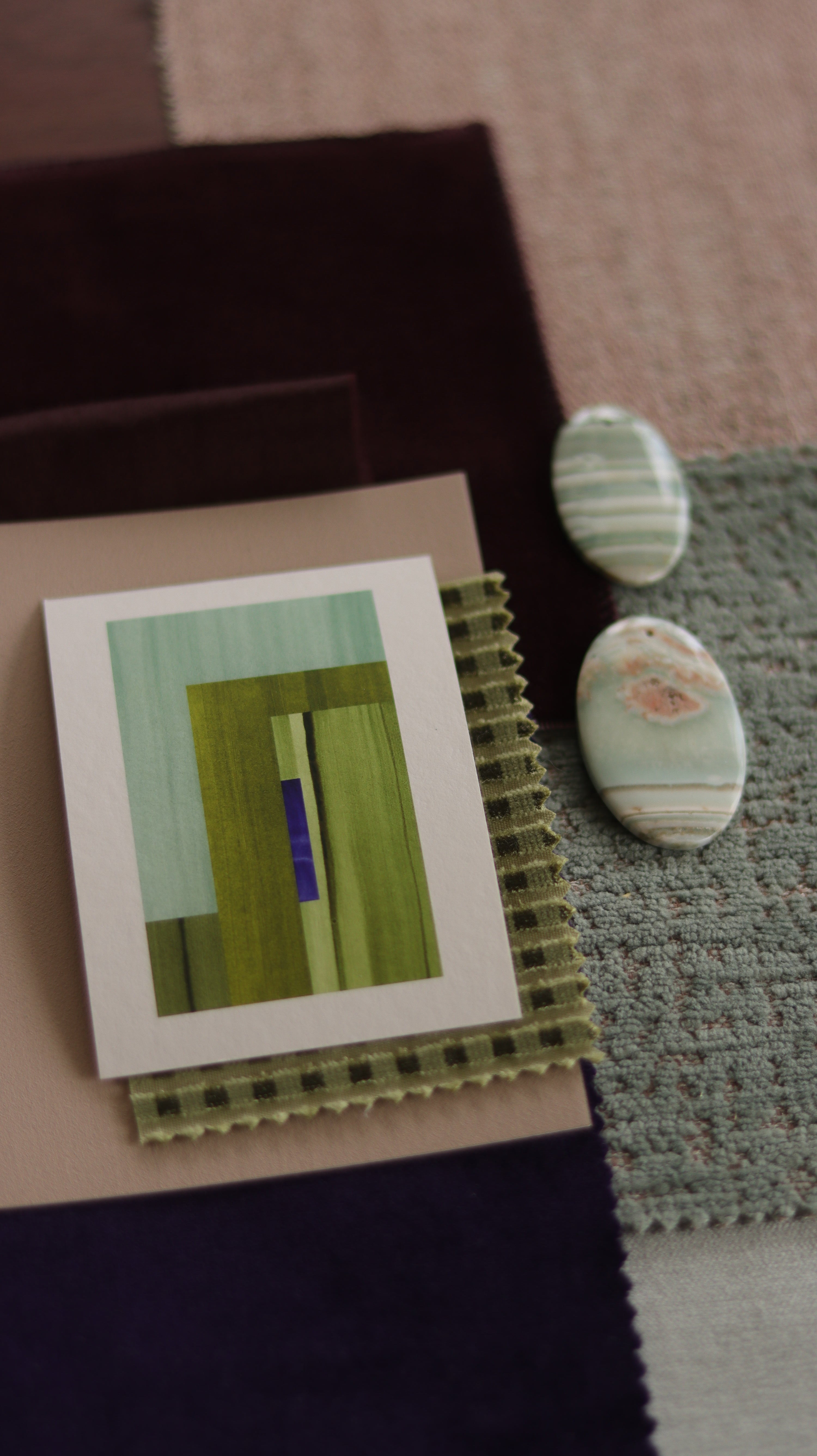 Small abstract art print sample with moss green, turquoise and blue colours, laying on top of fabric swatches for interiors colour inspiration.