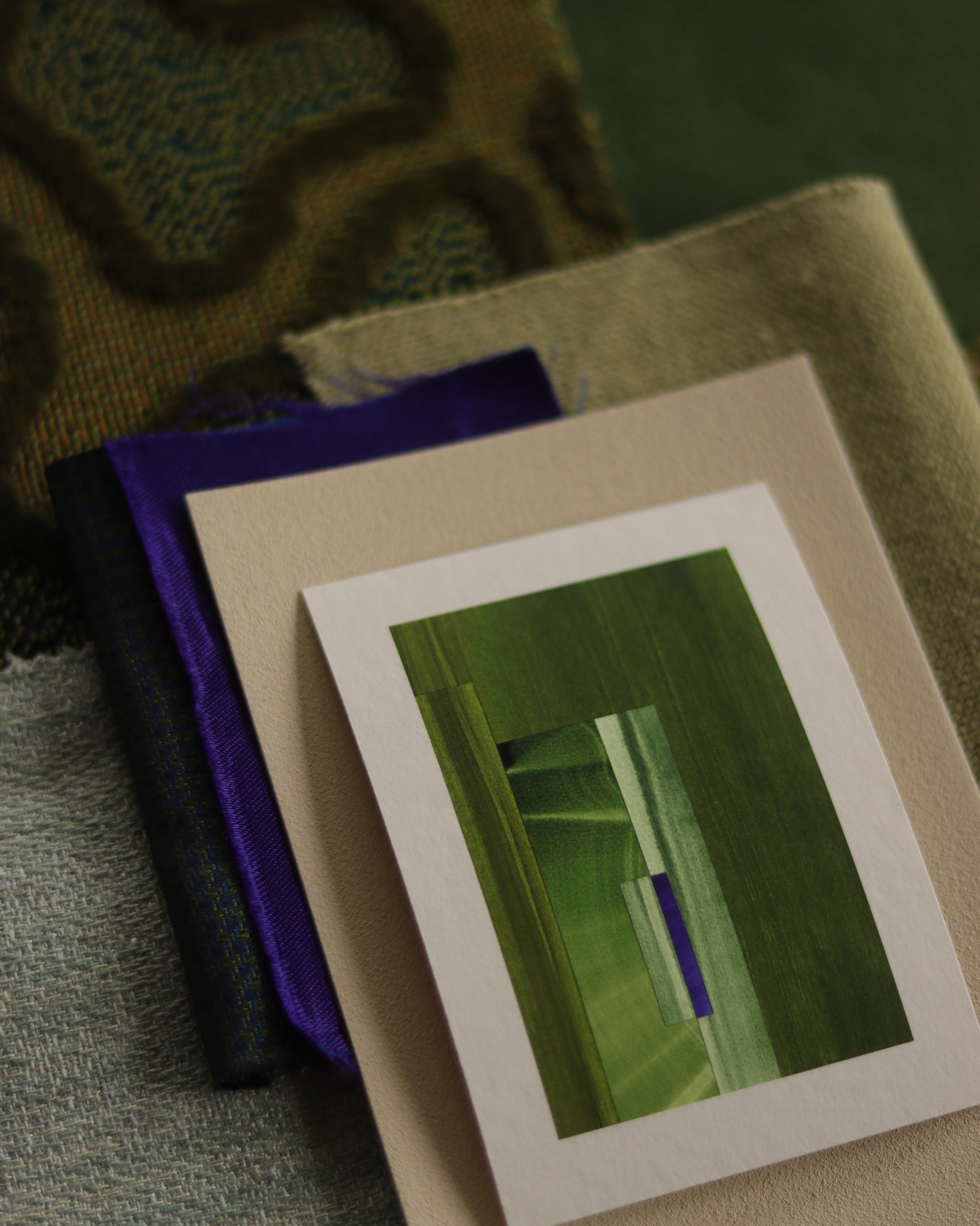 Small geometric abstract art print sample with moss green, sage green and blue colours, laying on top of fabric swatches for green interiors colour inspiration.