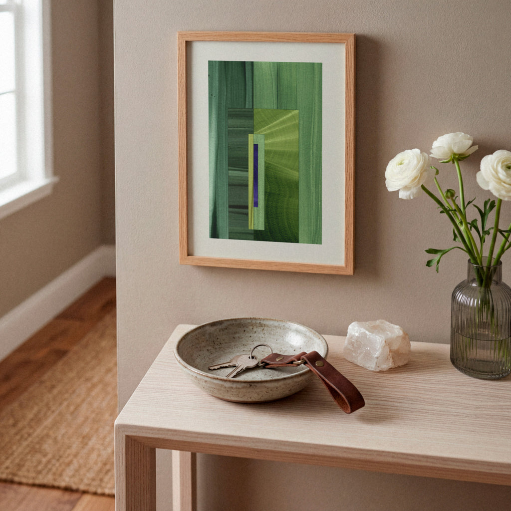 Framed green abstract artwork on a white oak console table, in a modern hallway, with a case of white flowers